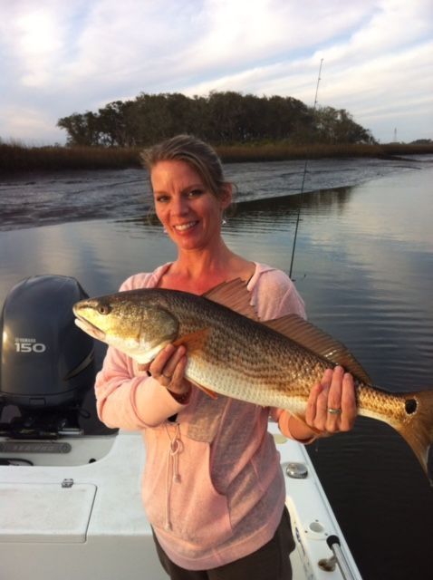 Woman holding a redfish on a boat in a marshy area; she is smiling.
