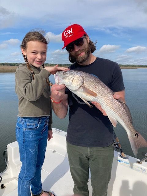A man and child on a boat with a caught fish. The man holds the fish, and the child points.