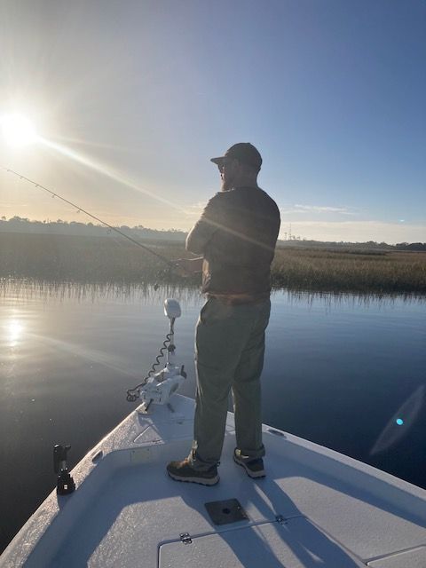 Man fishing from a boat at sunrise, casting a line in calm water.