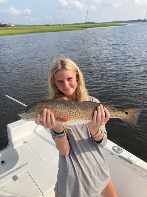 Woman on boat holding a redfish, smiling. Water and marsh in the background.