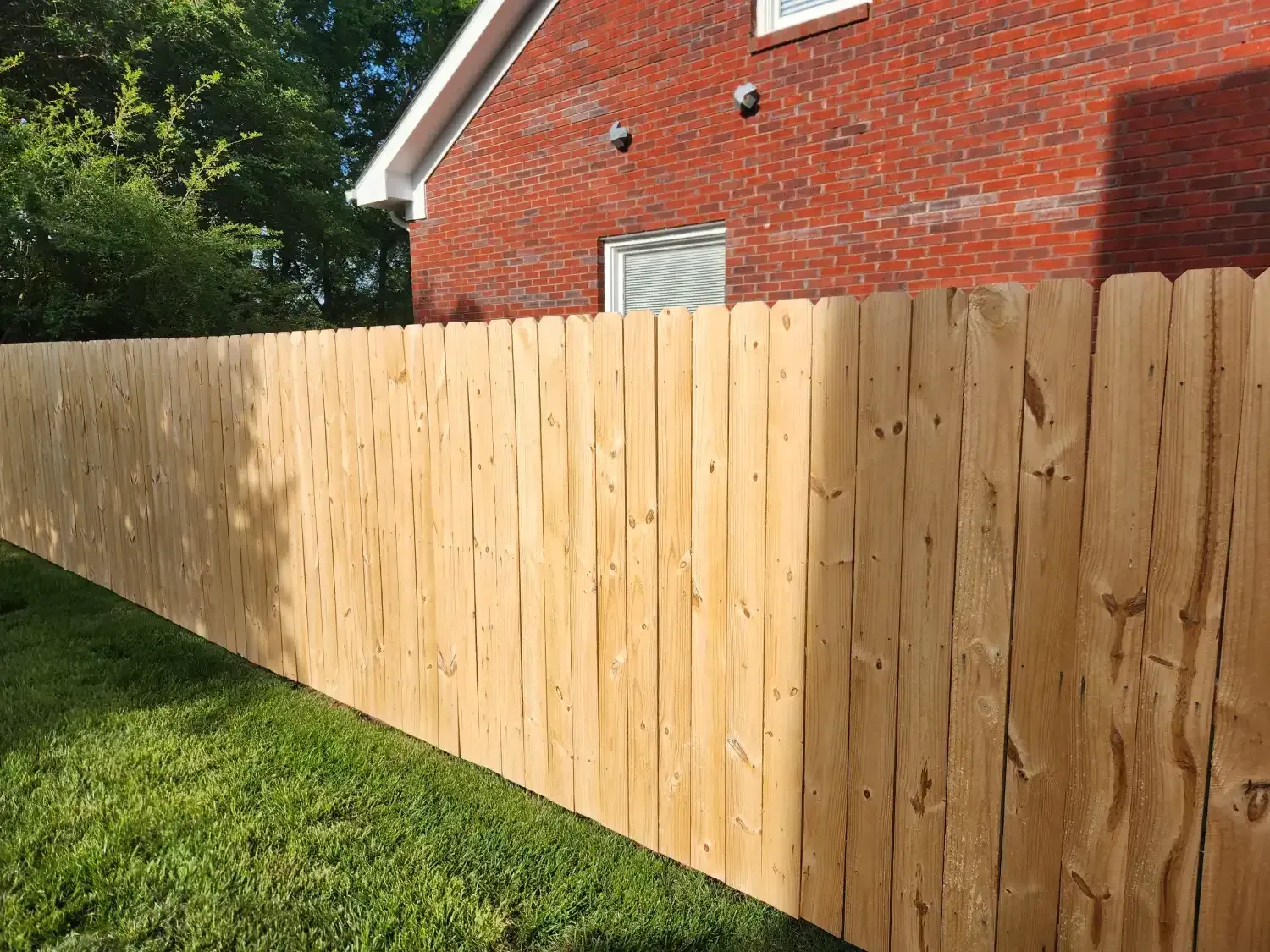 New wooden fence along a red brick house beside a grassy yard