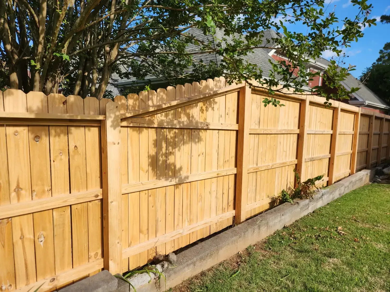 Freshly installed wooden privacy fence beside a grassy yard and concrete driveway under a blue sky