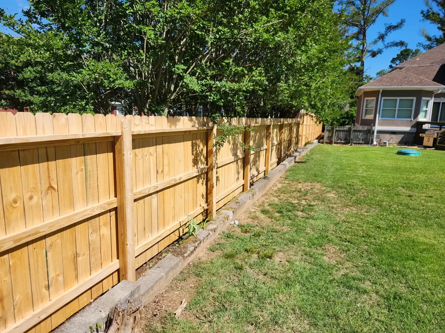 Wooden privacy fence along a grassy backyard beside a house under a clear blue sky