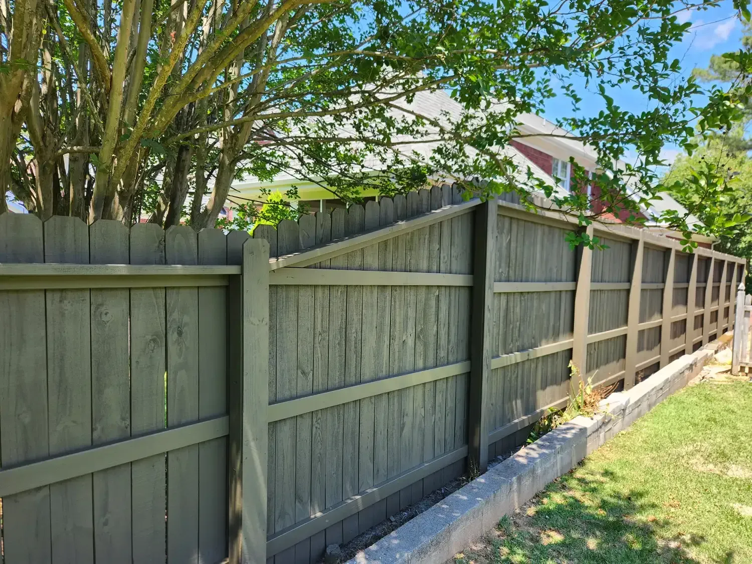 Weathered wooden fence beside a grassy yard with trees and a house in the background