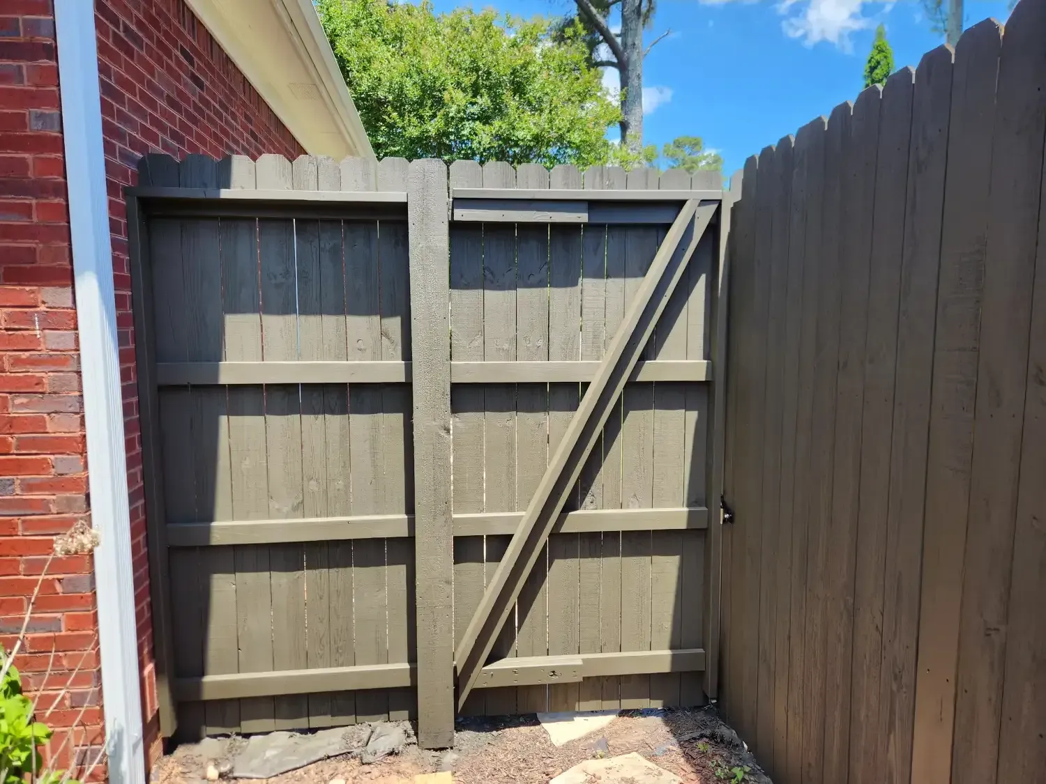 Wooden backyard gate between a brick wall and fence, with blue sky above.