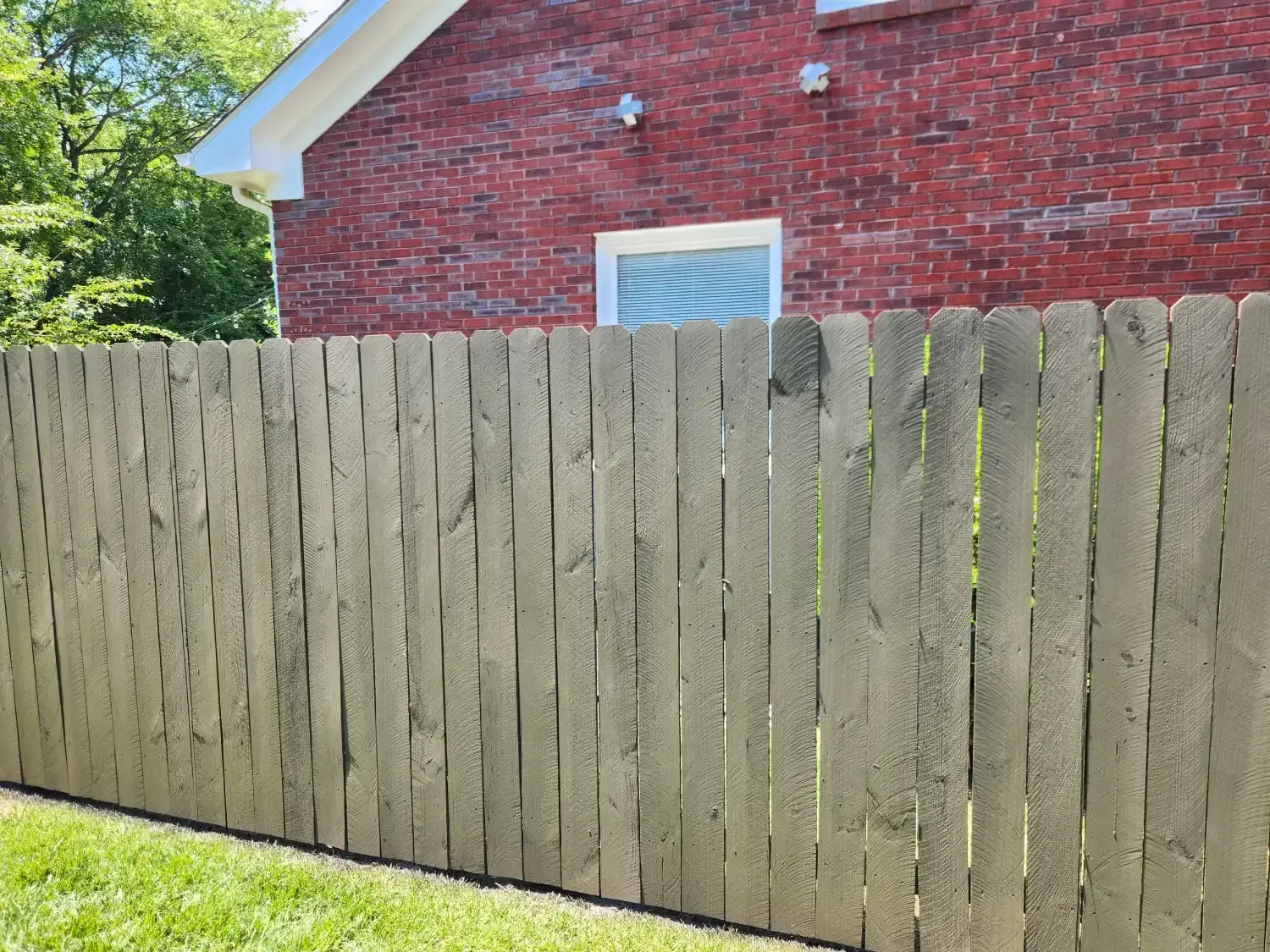 Weathered wooden fence in front of a red brick house with a white-trimmed window.
