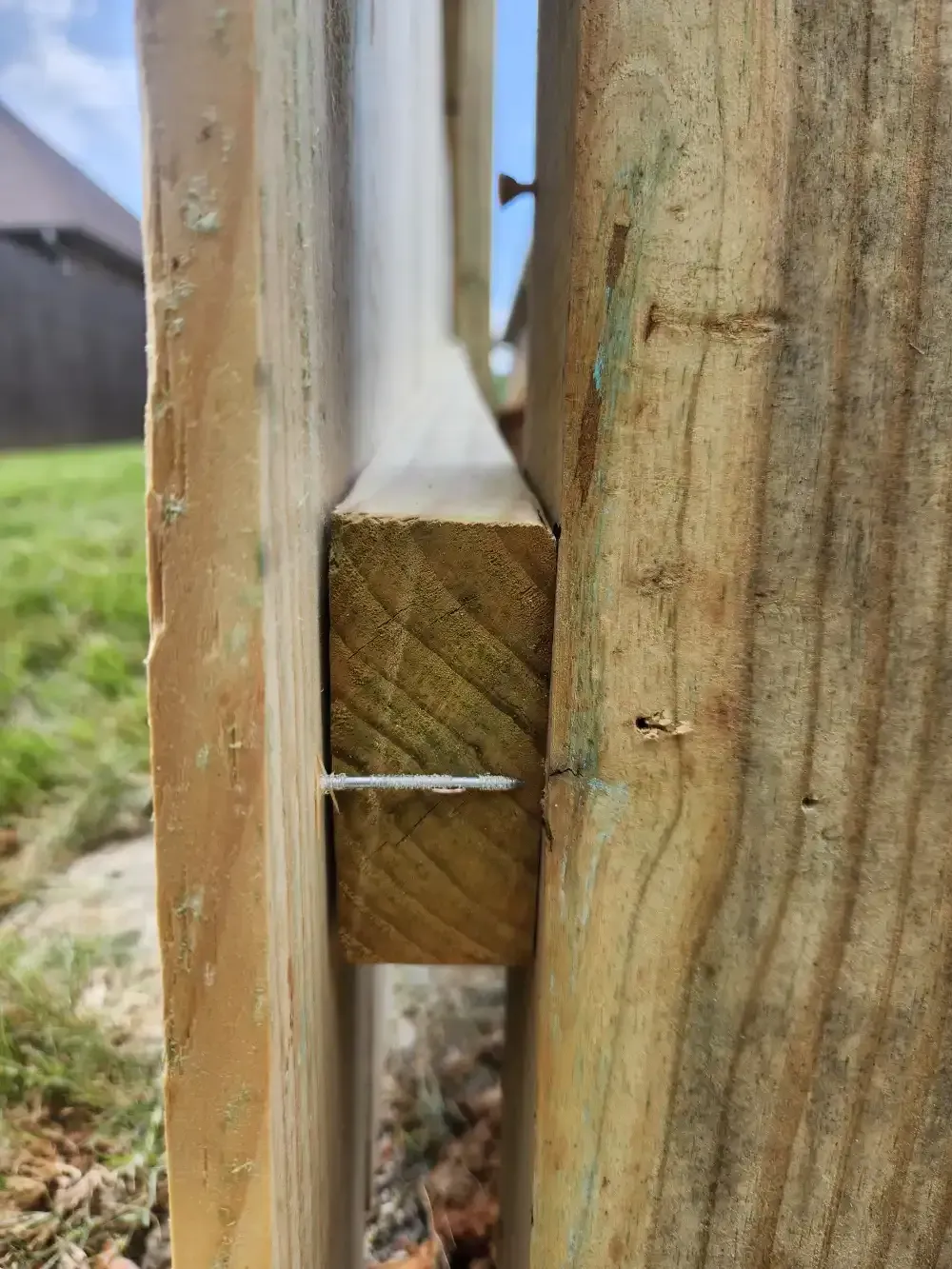 Close-up of a wooden fence joint with a metal nail or screw, outdoors on grass.