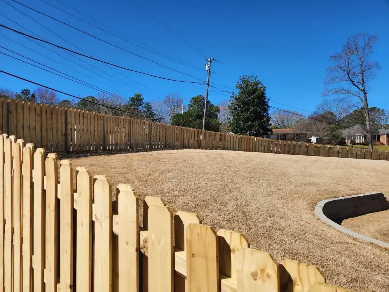 Wooden fence beside a beige landscaped slope under a clear blue sky