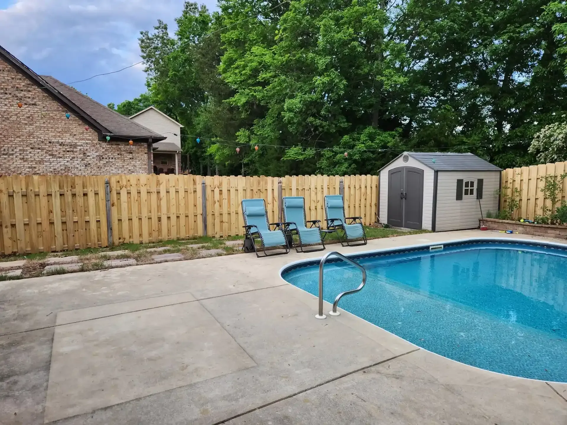 Backyard pool with patio, lounge chairs, and a storage shed beside a wooden fence