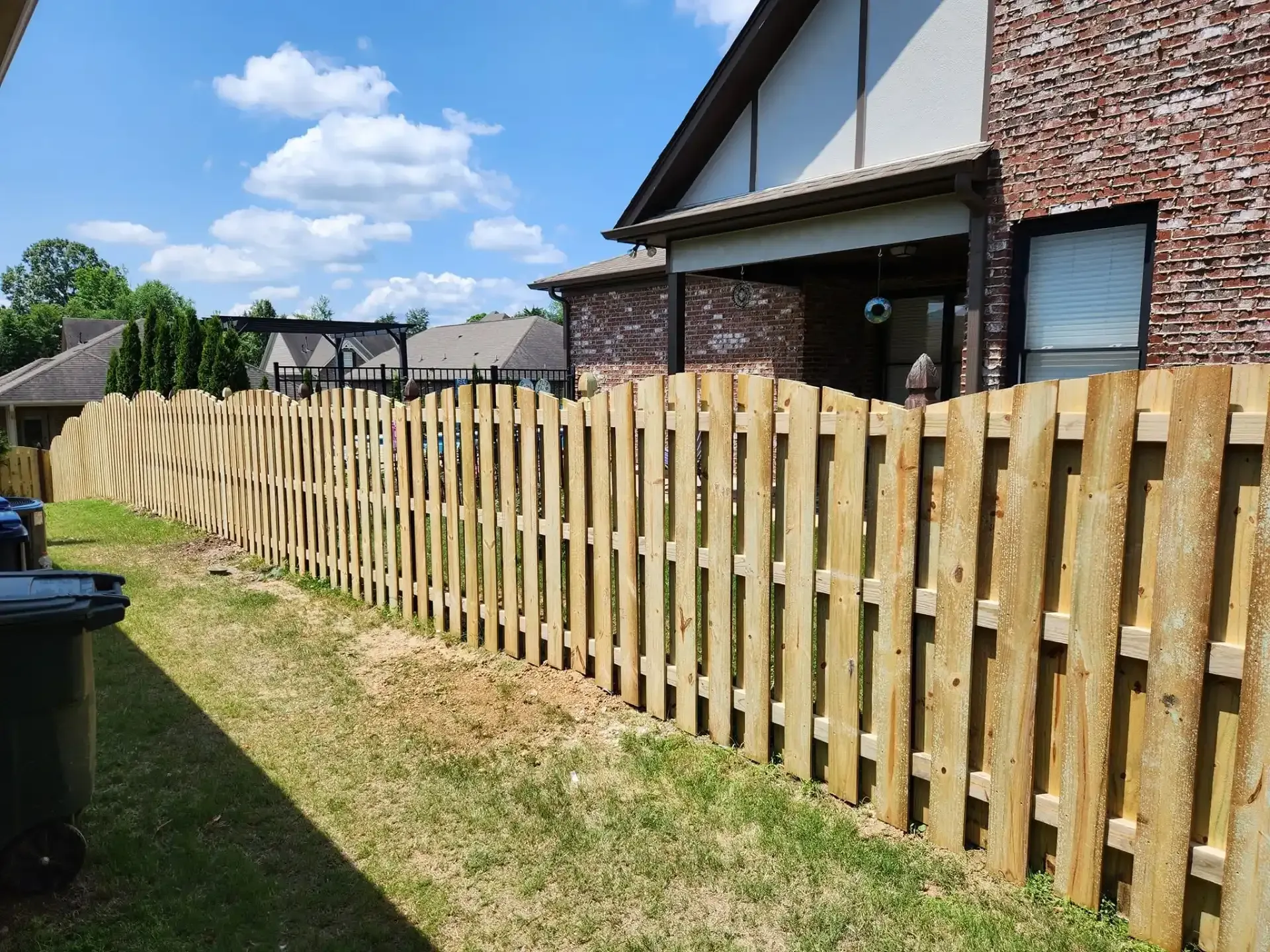 Wooden backyard fence beside a brick house on a sunny day