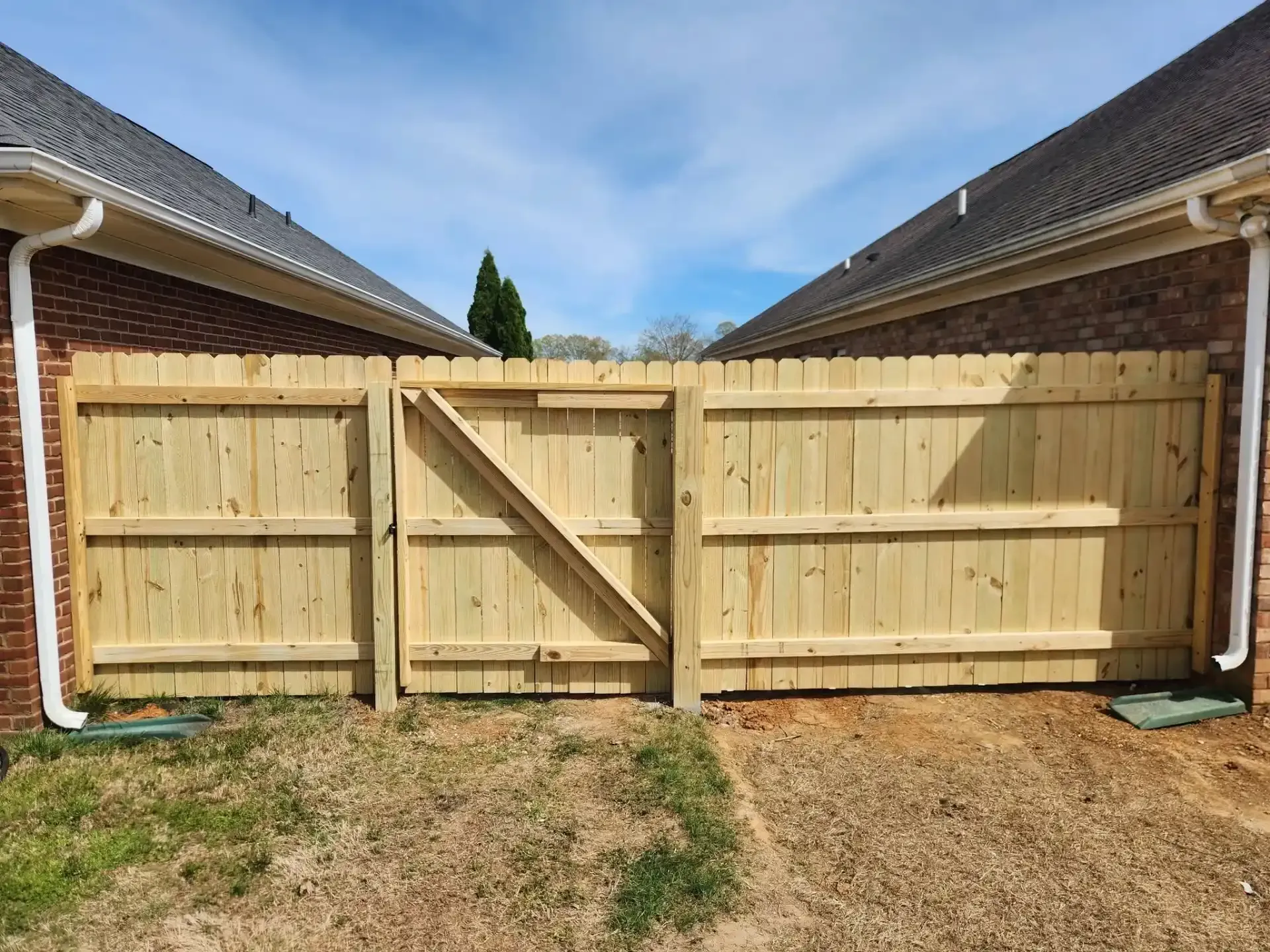 Wooden backyard gate between two brick houses, centered in a fenced driveway.