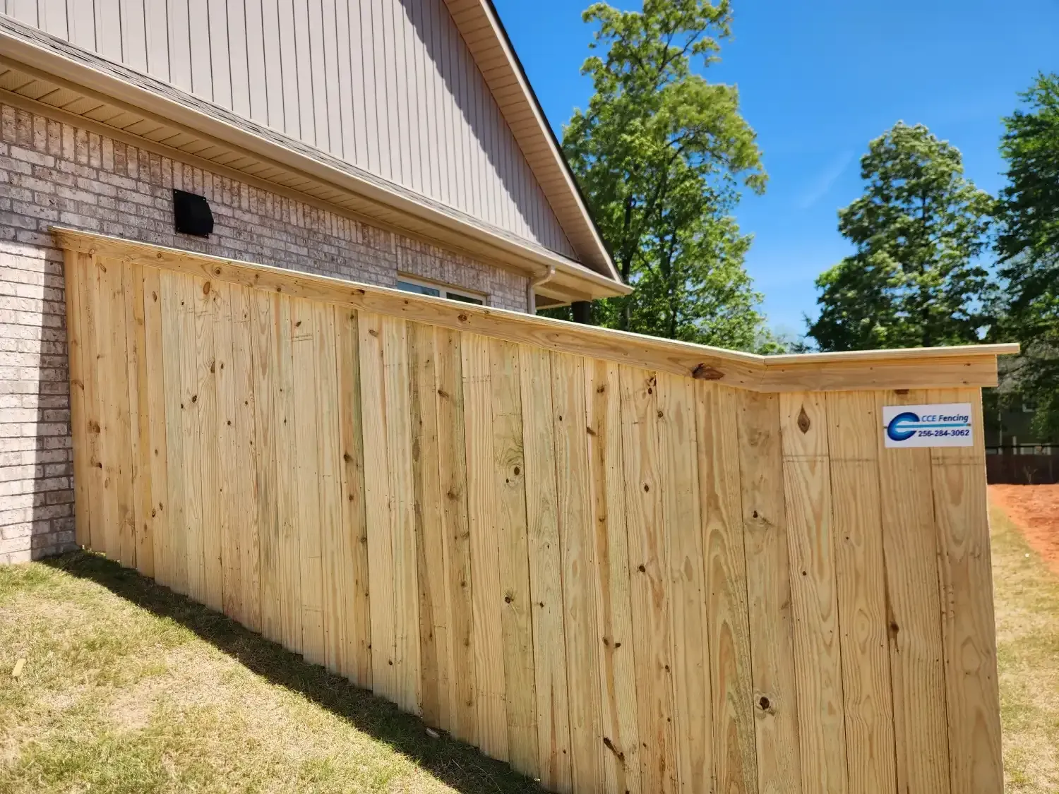 Wooden privacy fence beside a brick house under a clear blue sky
