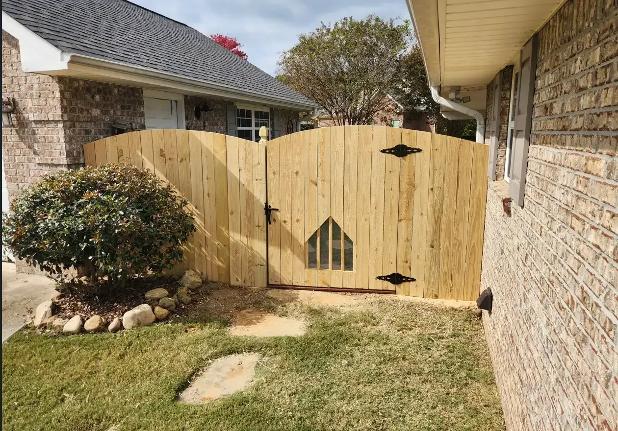 Wooden gate between brick houses, with a small pet door and lawn in front.