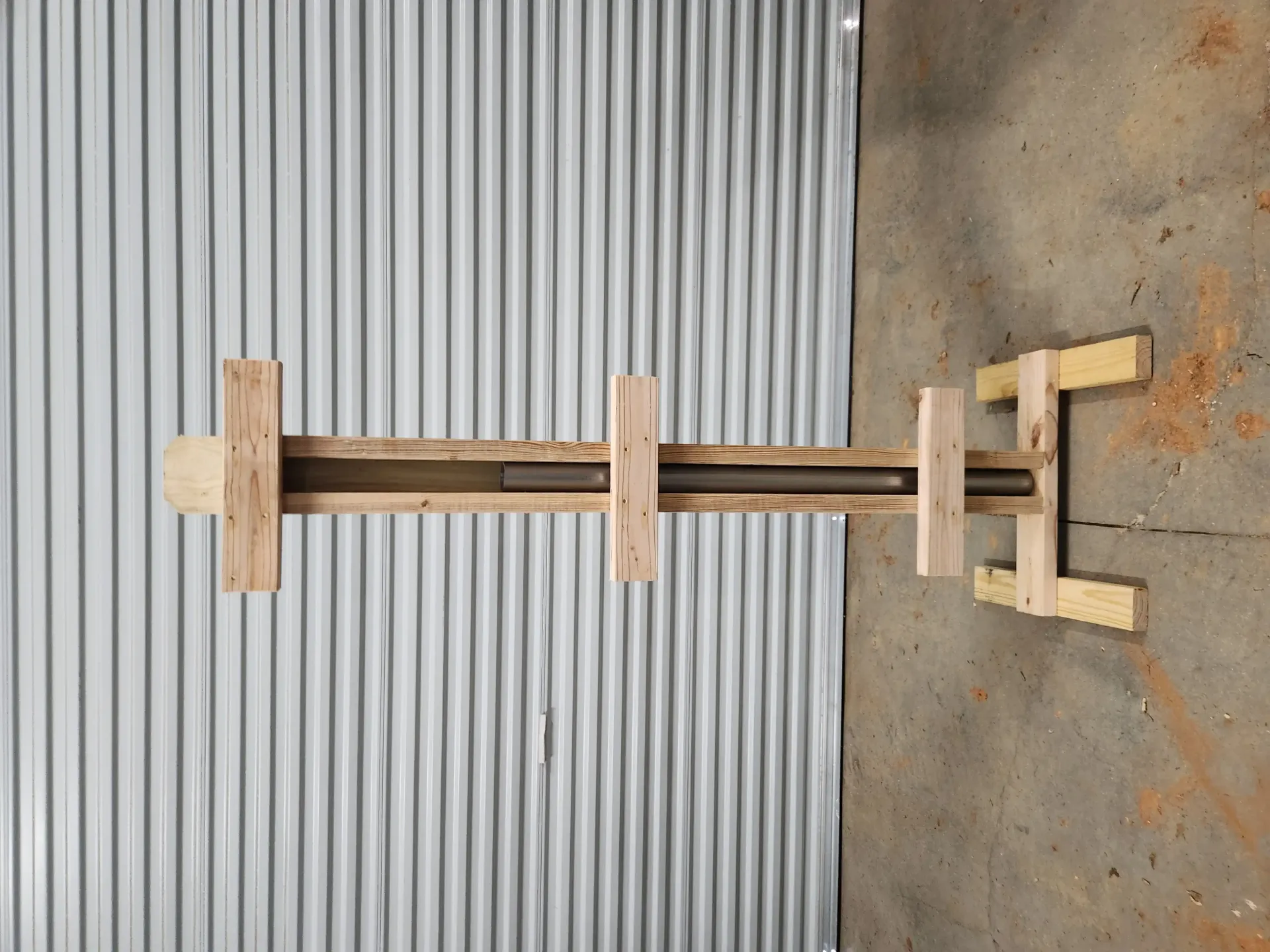 Wooden frame with metal rods and clamps lying on corrugated metal and concrete floor.