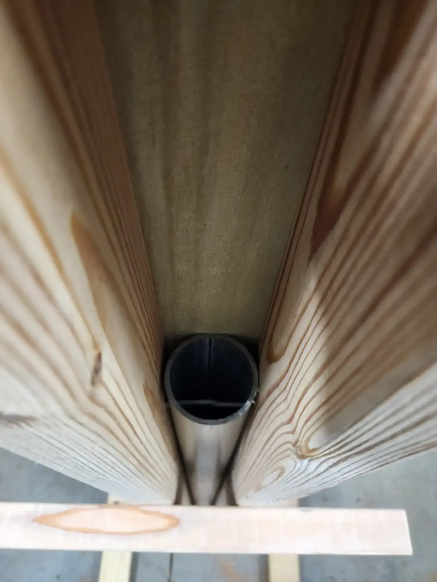 Top-down view of a black pipe between two wooden boards, with a white plank across the bottom.