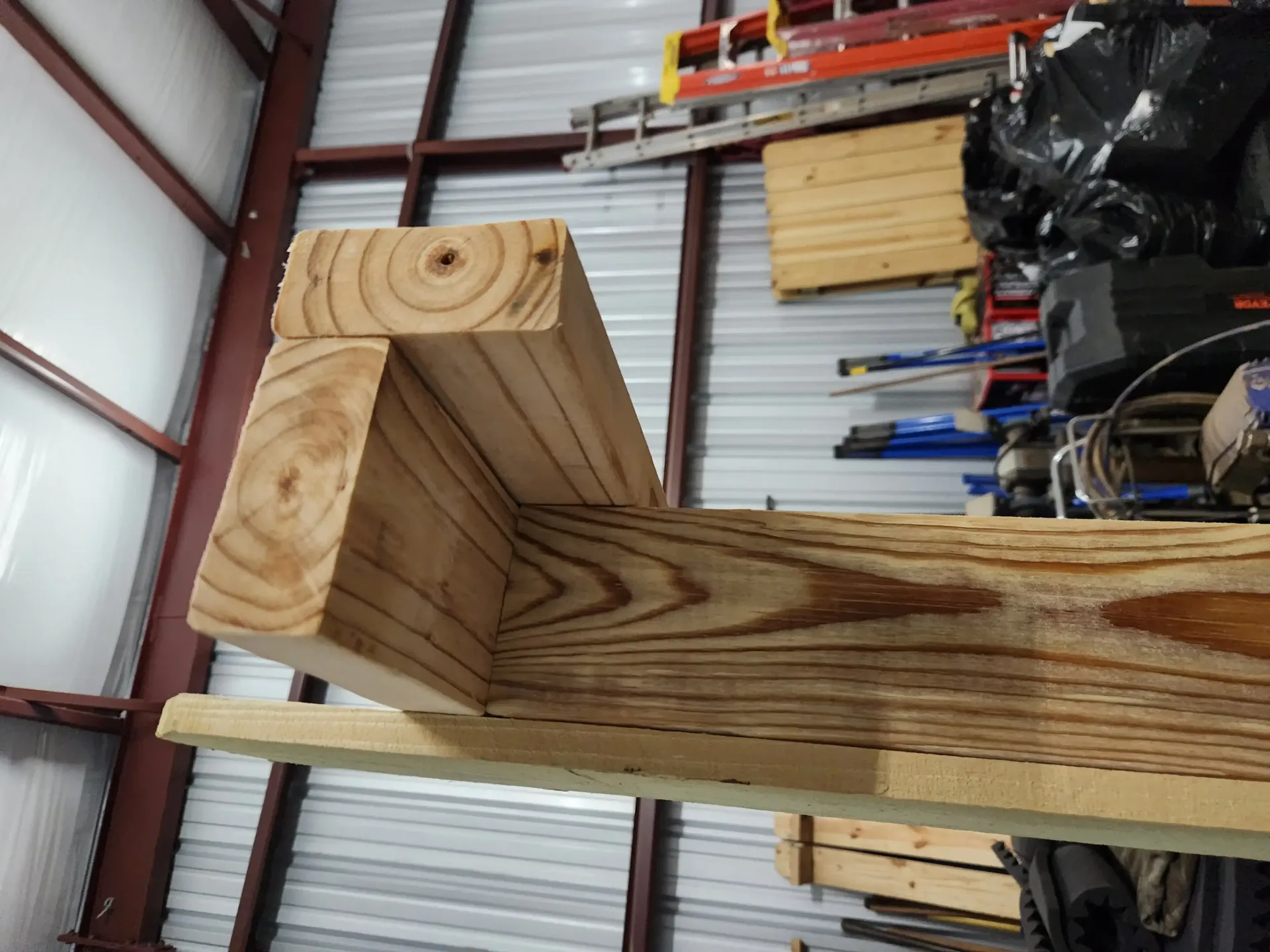 Close-up of a wooden bracket or shelf support in a workshop, with visible grain and metal shelving in the background