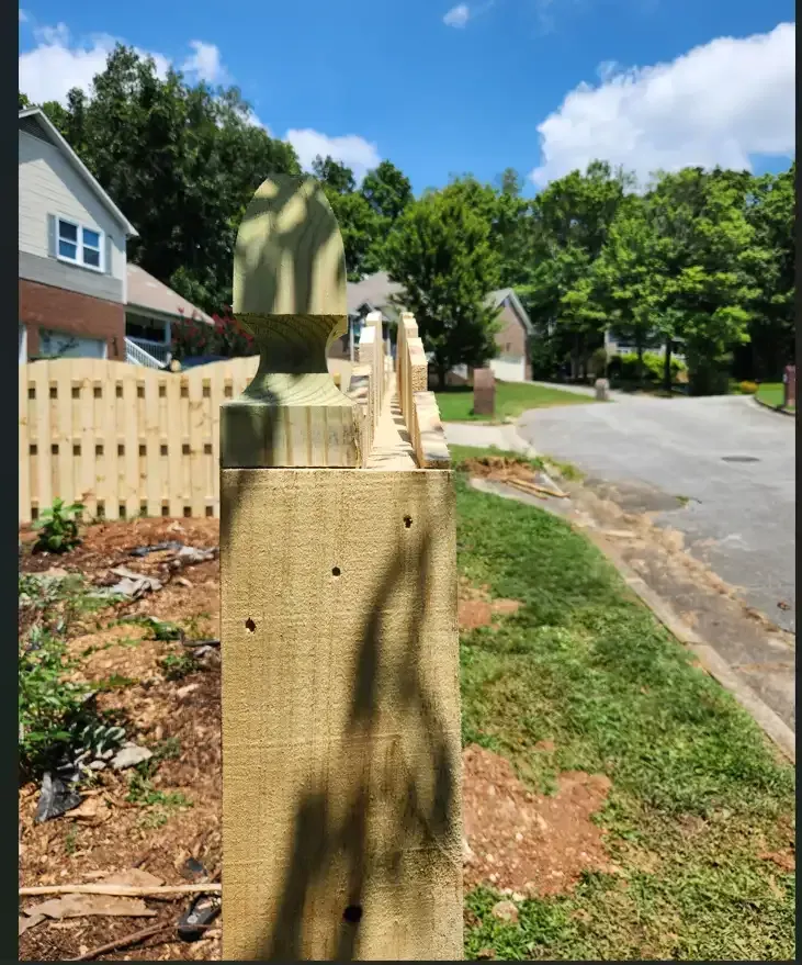 Wooden fence posts and a sidewalk along a sunny suburban street with houses and trees