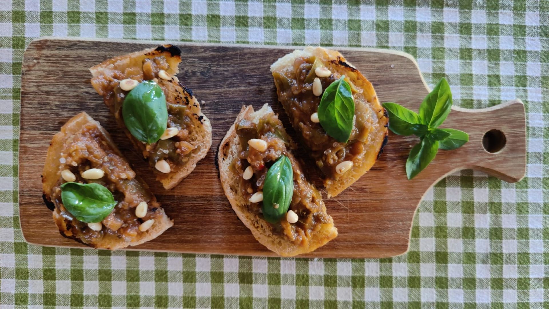 Four toasted crostini topped with a vegetable tapenade of aubergines, garnished with fresh basil