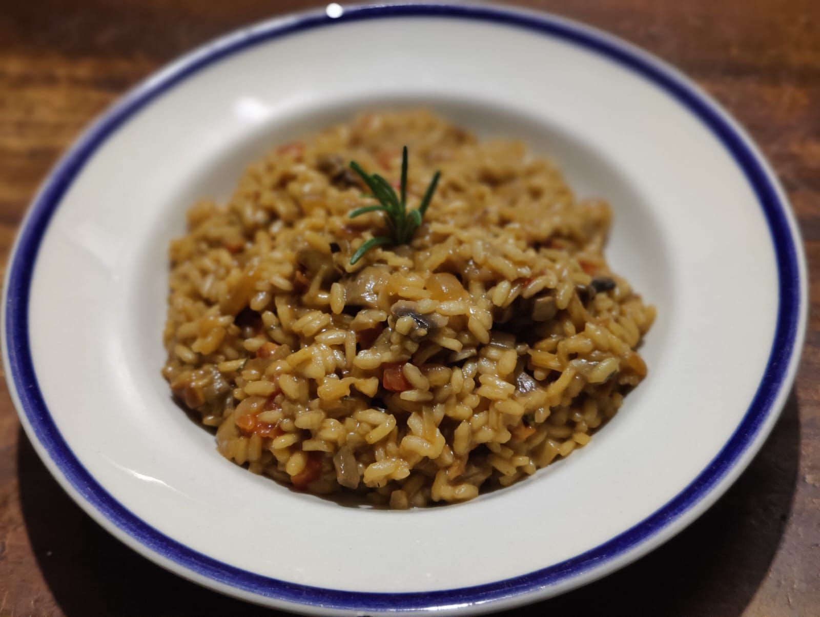 Creamy porcini risotto with diced veggies and rosemary on a white plate with a blue rim