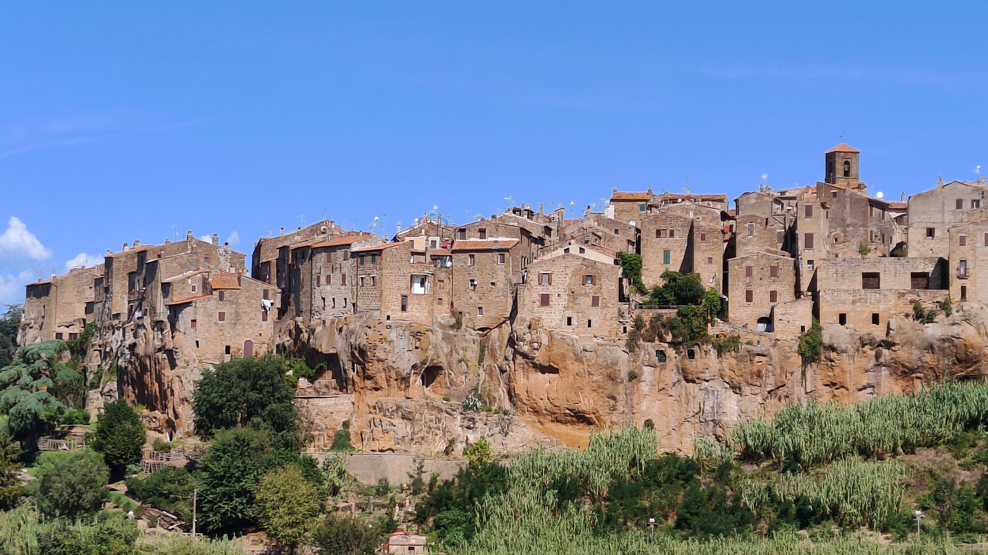 Stone hilltop village perched on rocky cliff with bell tower, tiled roofs and olive groves