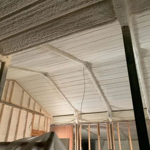 Interior of a building with spray foam insulation on the ceiling and walls. Wooden beams are visible.