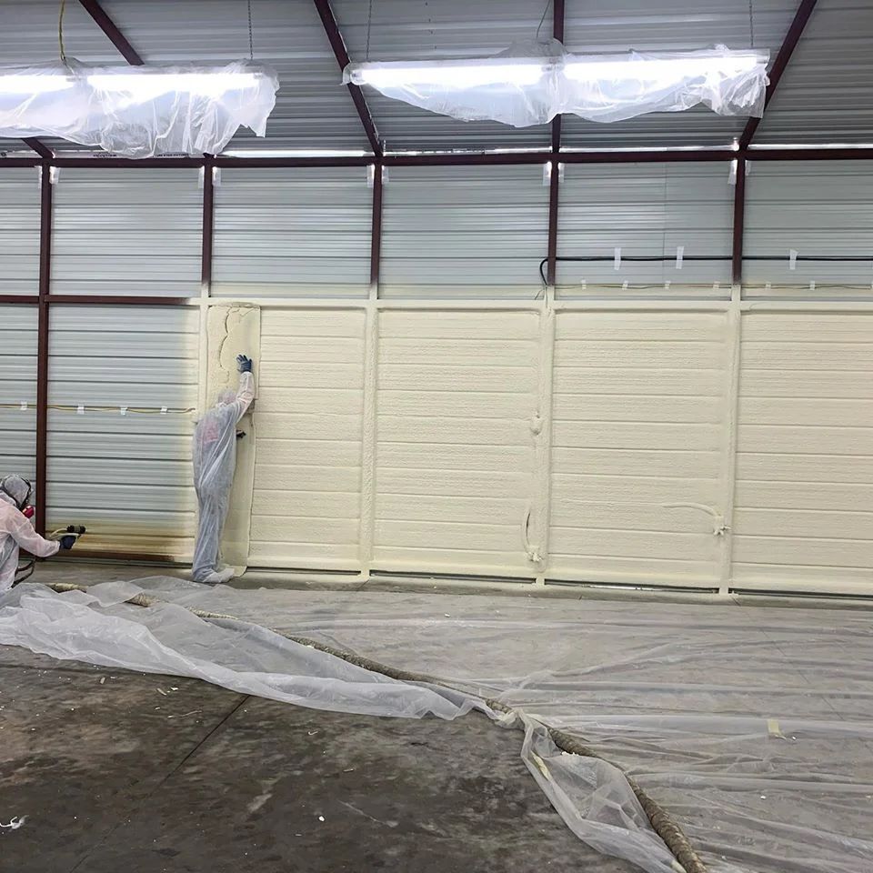 Two people spraying foam insulation onto a wall inside a building.