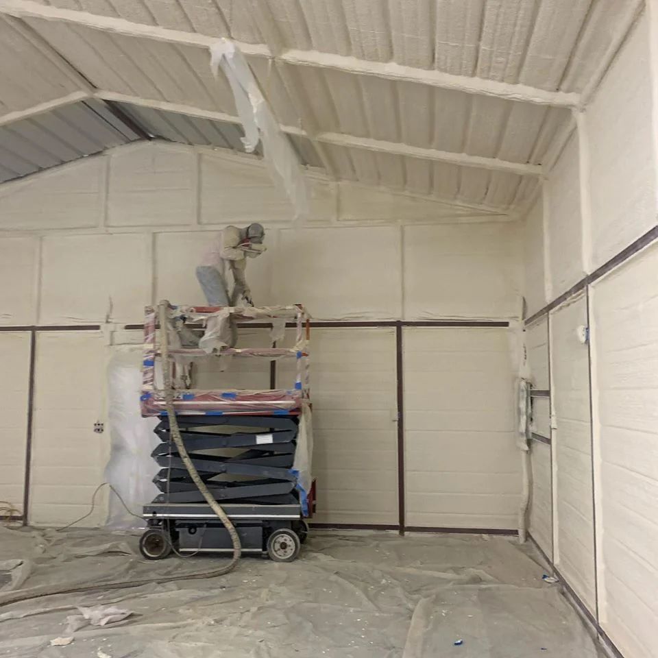Person spraying insulation on walls and ceiling inside a building.