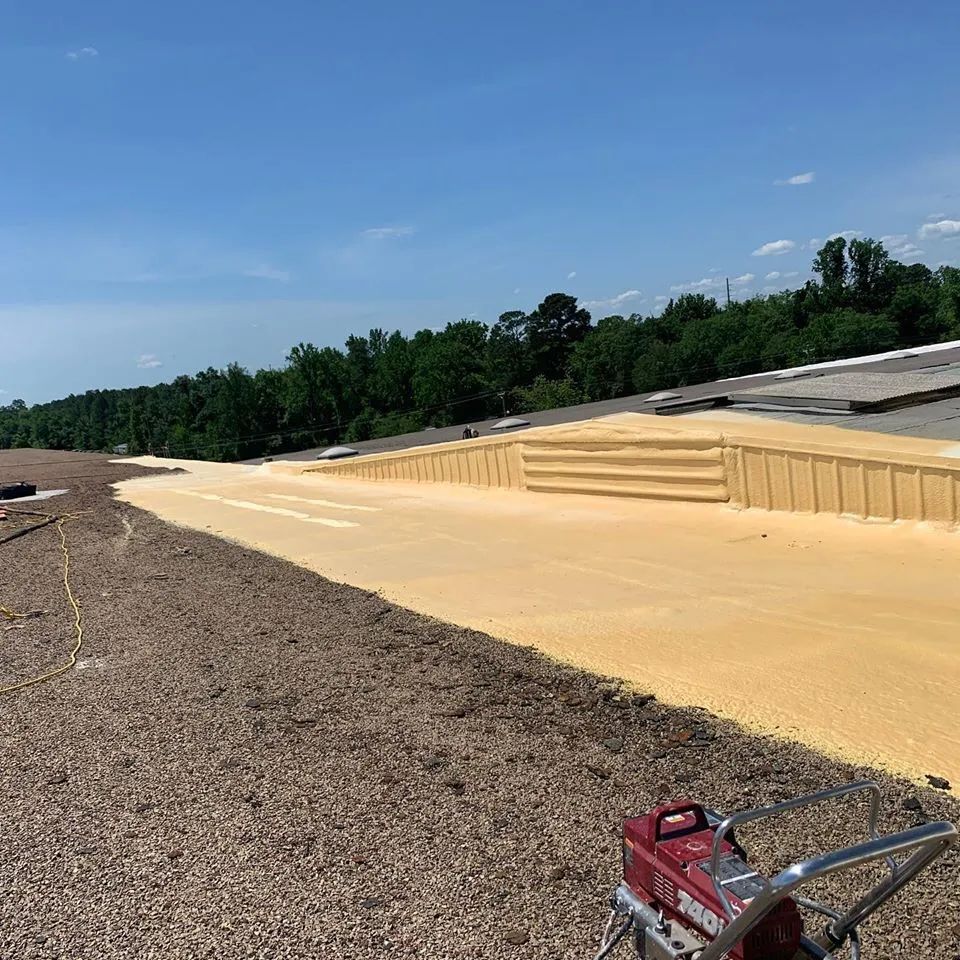 Spray foam roofing installation on commercial building with blue sky and trees in the background.