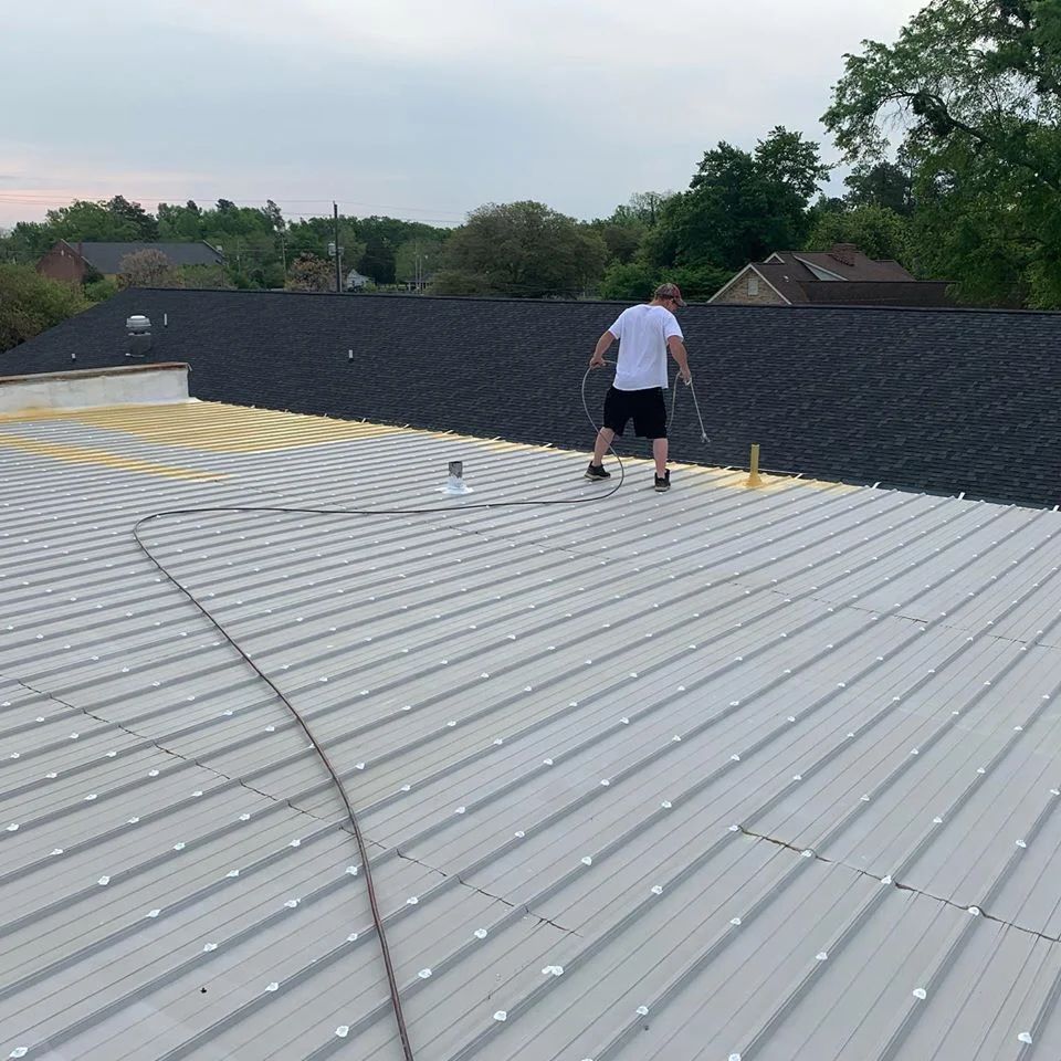 Person on a corrugated metal roof painting yellow lines, another roof in the background.
