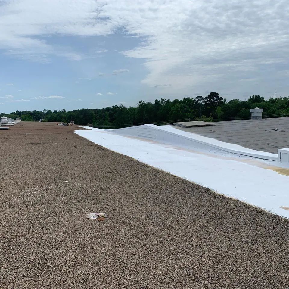 Gravel-covered flat roof with a large section covered in white material; trees and sky in the background.