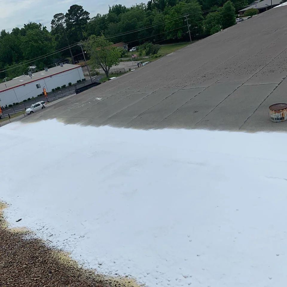 A white coating being applied to a large, gray, flat roof.