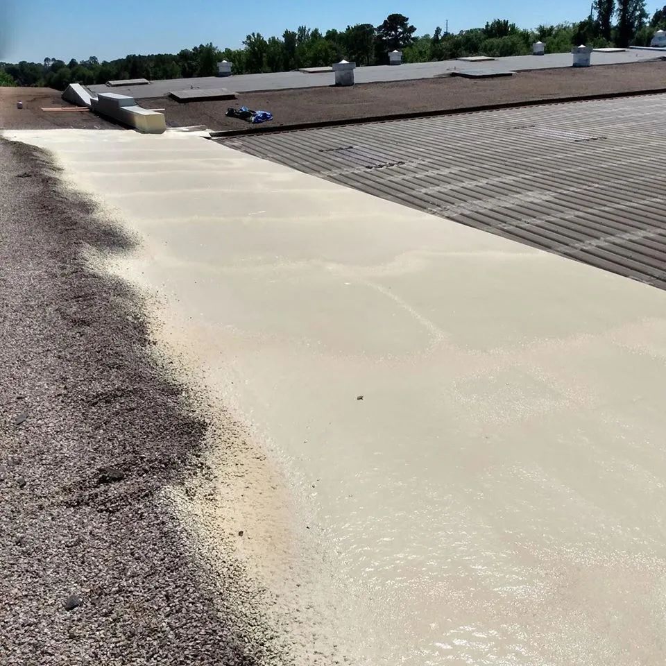 Roof with tan foam coating next to gravel, under a blue sky.