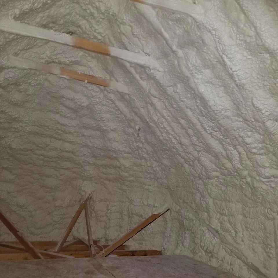 Attic insulated with light tan spray foam, covering the walls and rafters.