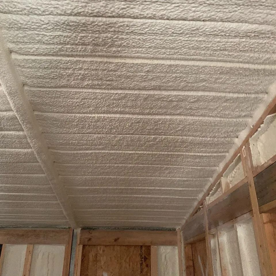 Foam insulation applied to a ceiling and adjacent walls in a wooden structure.