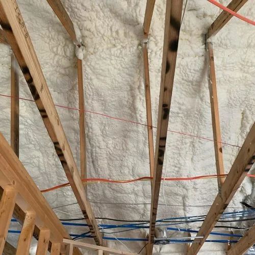 Wooden rafters with sprayed foam insulation; electrical wiring visible.