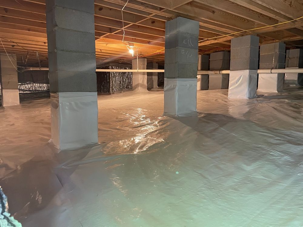 Crawl space covered in white plastic sheeting. Concrete block pillars support wooden floor joists.