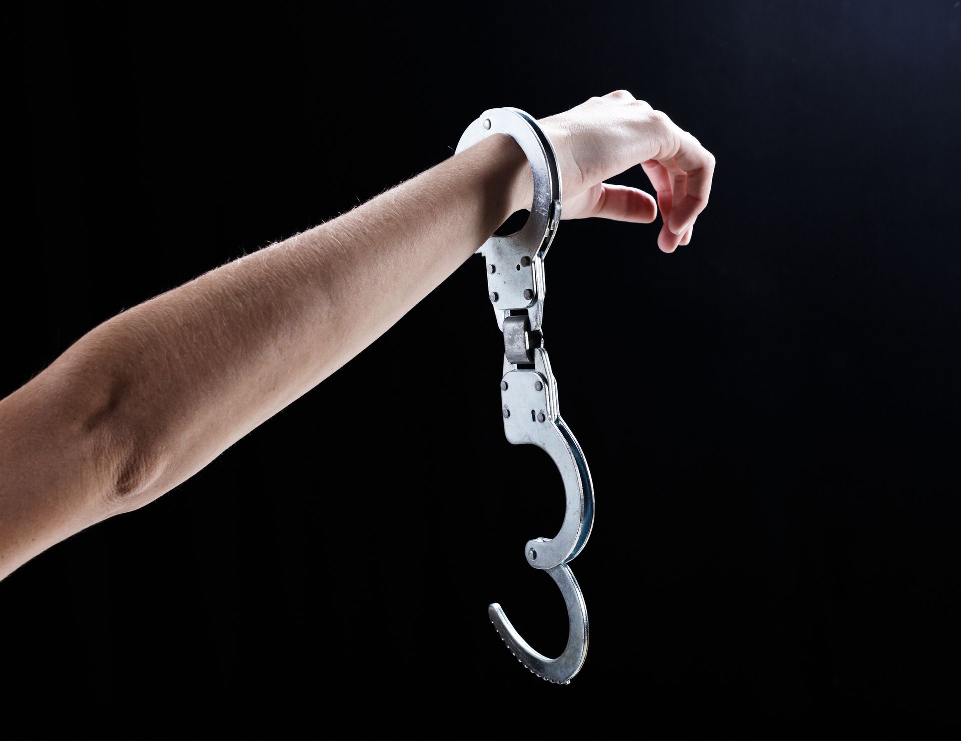 A woman's hand, holding up a hand wearing a single, open handcuff.