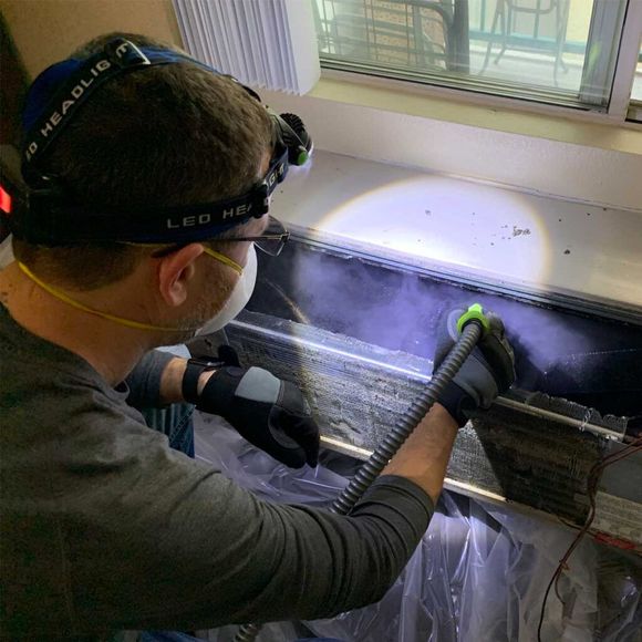 A man wearing a mask and gloves is cleaning a refrigerator with a hose.