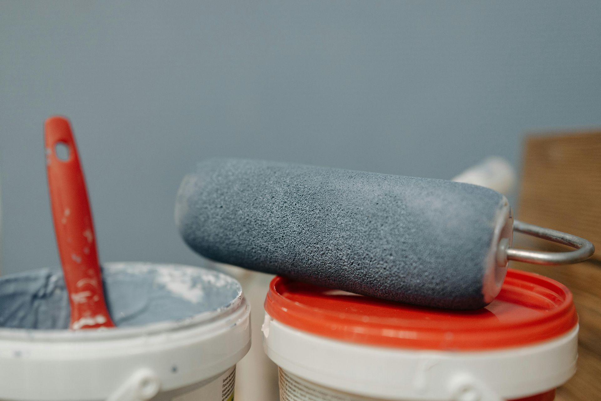 Paint roller on paint can, red handle in blue paint, blue background.