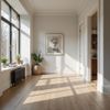 Hallway with sunlight streaming through a large window, artwork on wall, and a glimpse into a kitchen.
