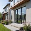 Modern two-story house with large windows, stone patio, and landscaped yard.