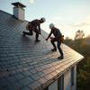 Two roofers in harnesses on a slate roof, repairing shingles under a bright sky.