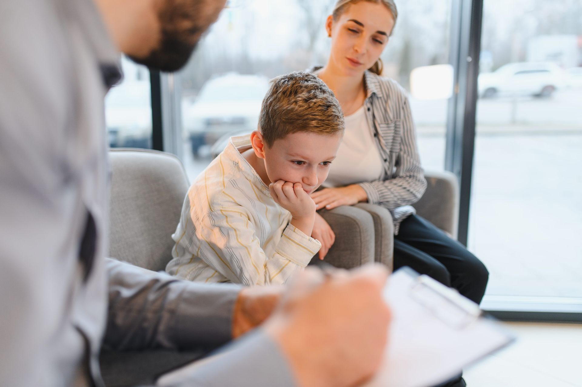 Family in counseling session, with a child listening while adults speak across a table.