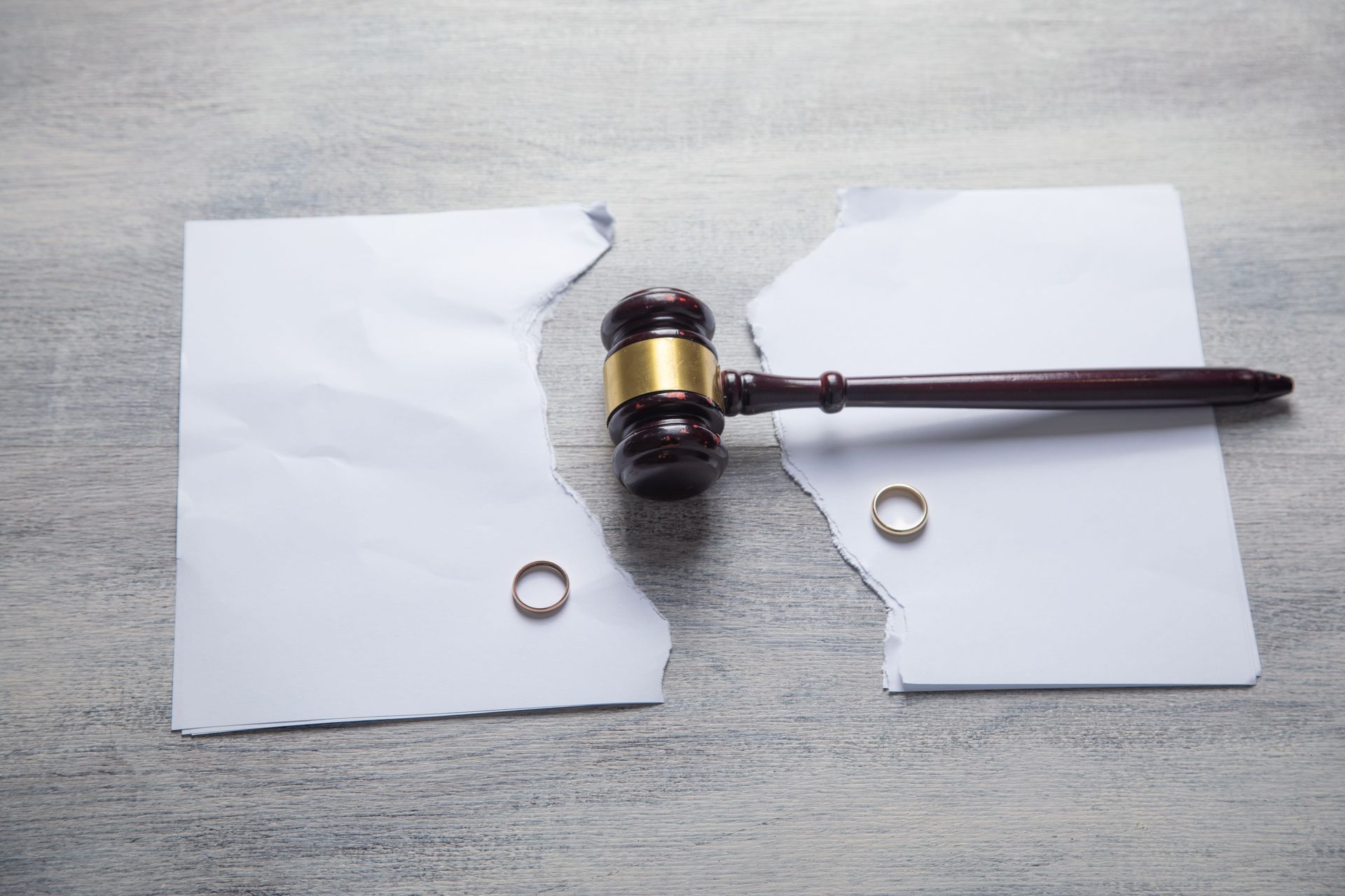 Two torn pieces of paper with a judge’s gavel and two rings on a gray surface