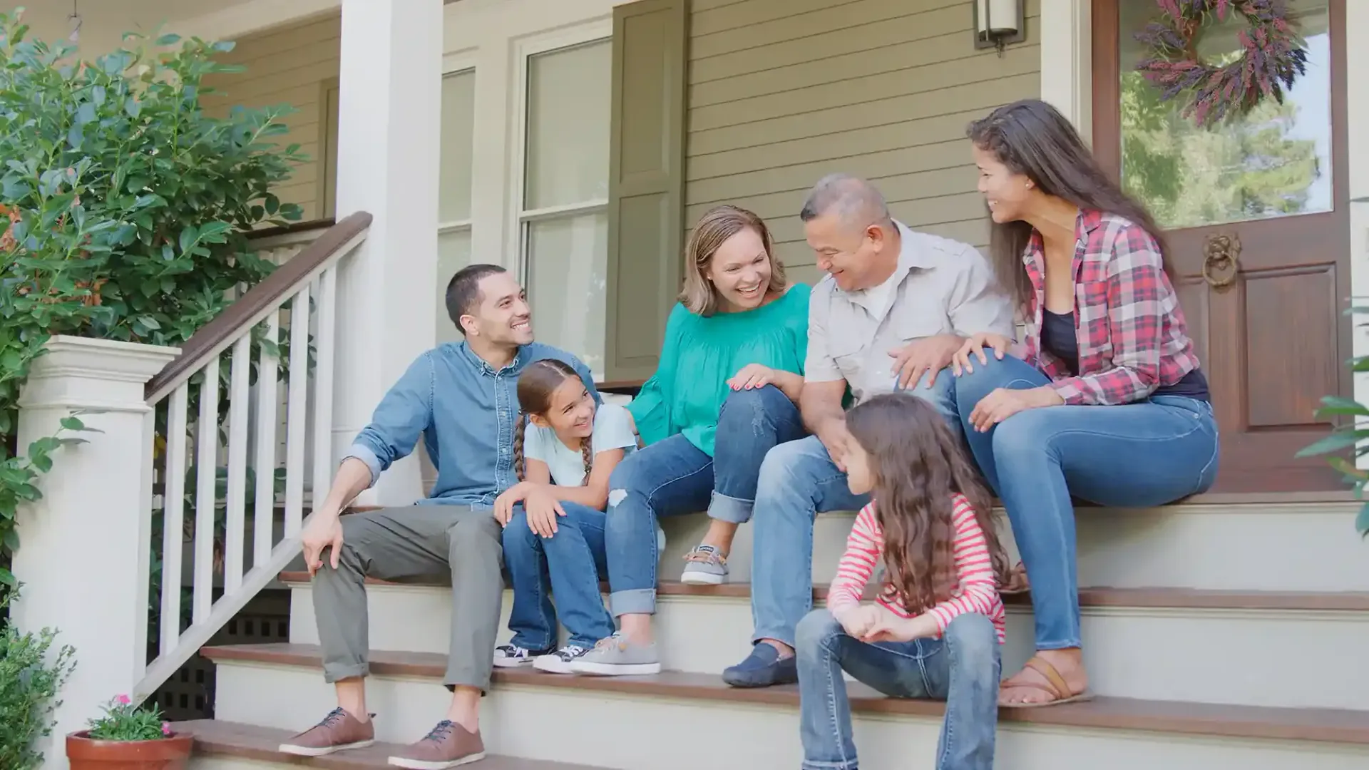 Family sitting together on front steps of a house, smiling and chatting outdoors