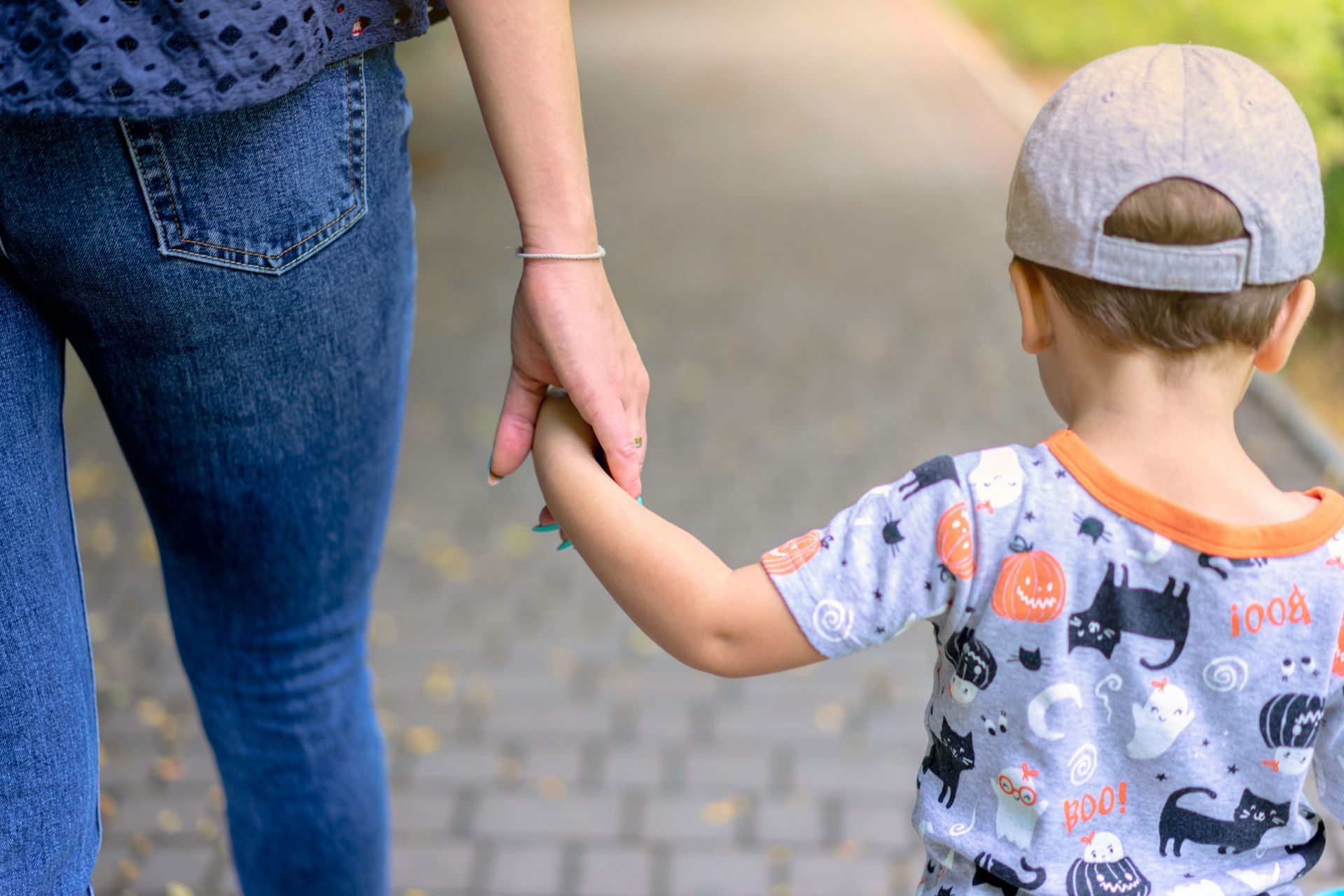 Adult and child holding hands while walking on a paved path