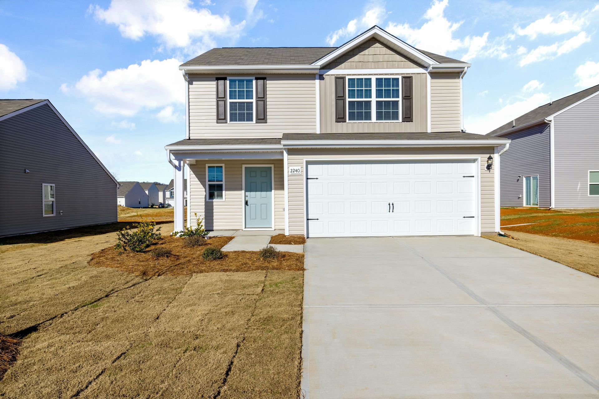 Two-story beige house with a white garage door and light blue front door on a sunny day.