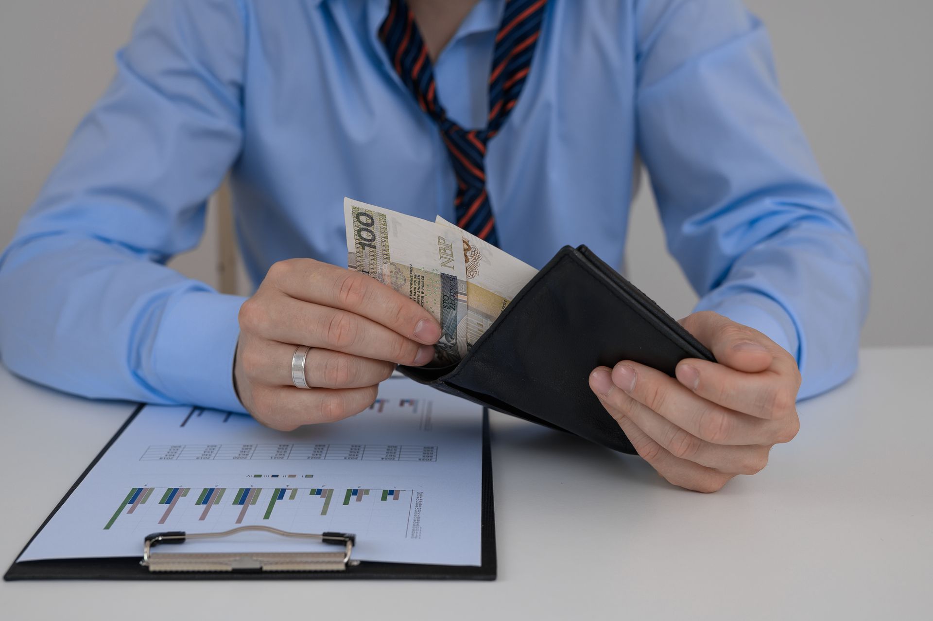Person in blue shirt holding a wallet with money over a document on a desk.