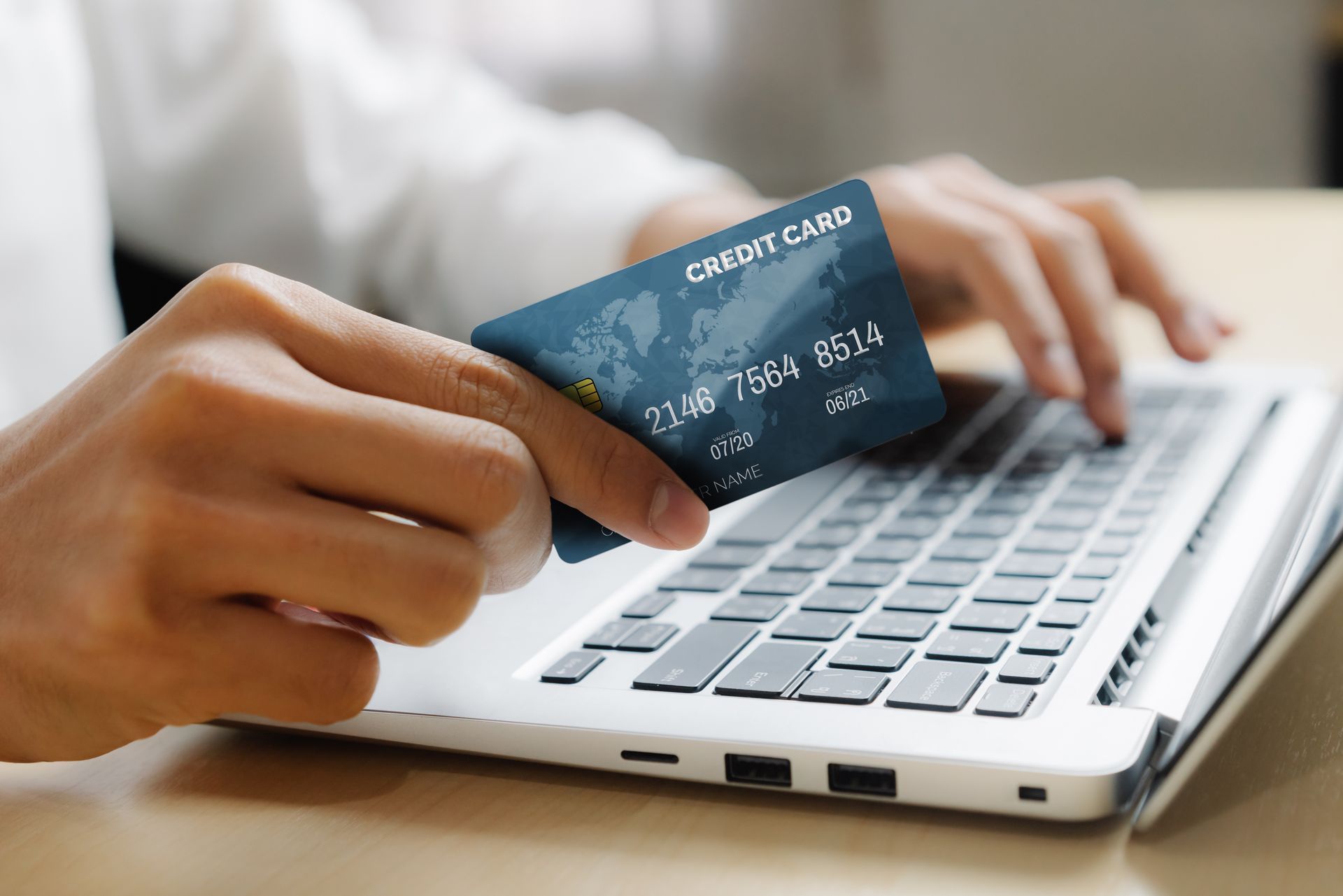 Person holding a credit card while typing on a laptop. Person holding a credit card while typing on a laptop.