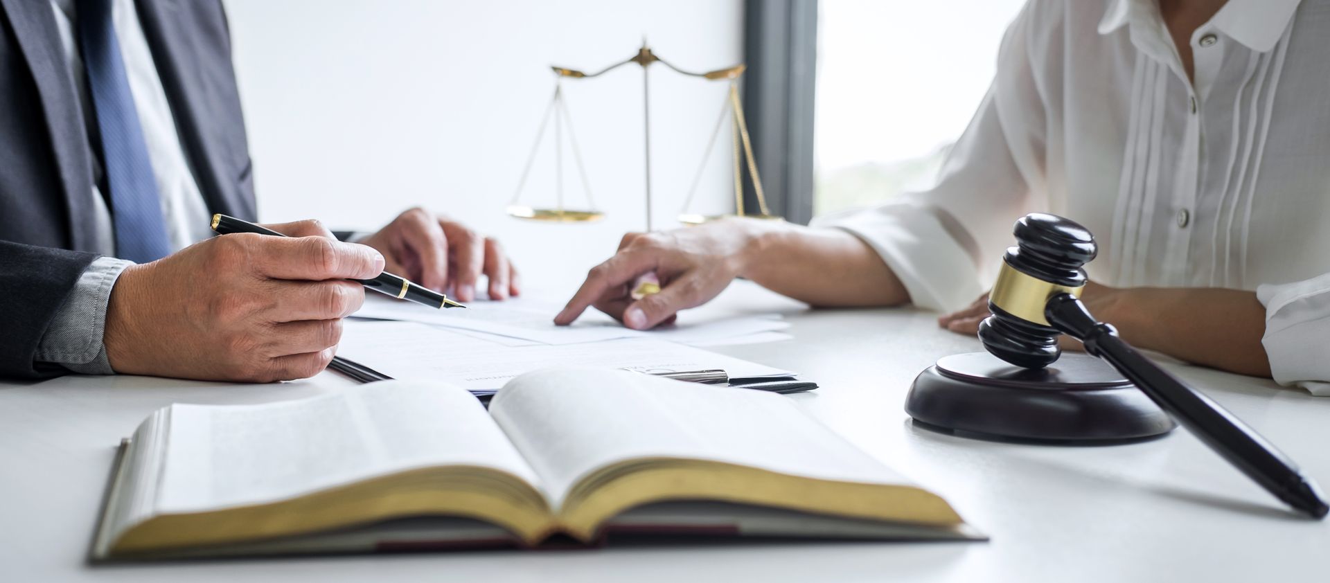 Two people reviewing documents at a table. A gavel, law book, and scales of justice are in the background. Two people reviewing documents at a table. A gavel, law book, and scales of justice are in the background.
